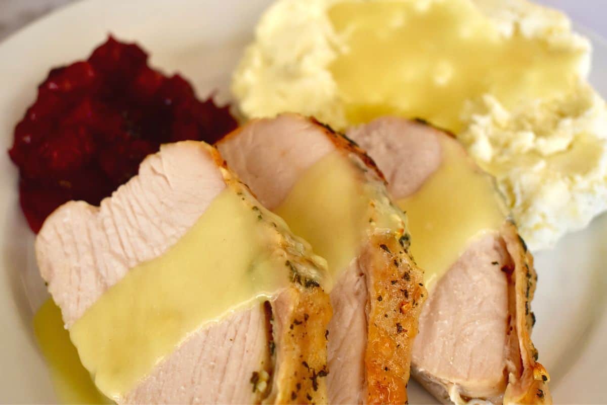 How to make slow cooker turkey breast with gravy on a white plate with cranberries and mashed potatoes. 