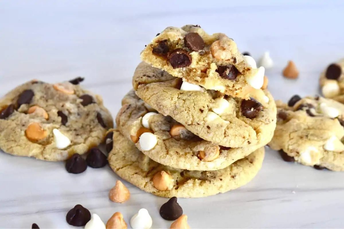 Triple Chocolate Chip Cookies stacked on each other on a white surface with chips scattered around them. 