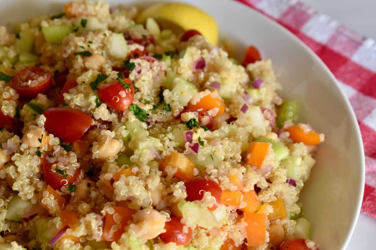 Quinoa Veggie Salad in a large white bowl with lemon wedges. 