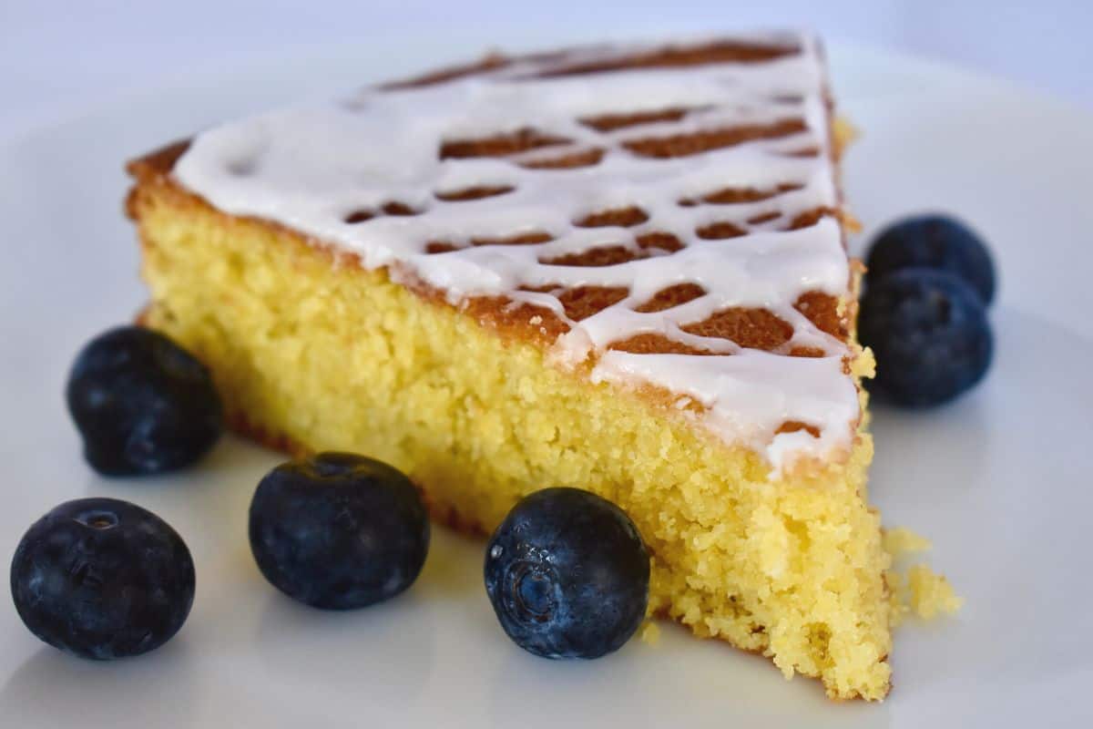 Lemon Polenta Cake slice on a white plate with blueberries. 