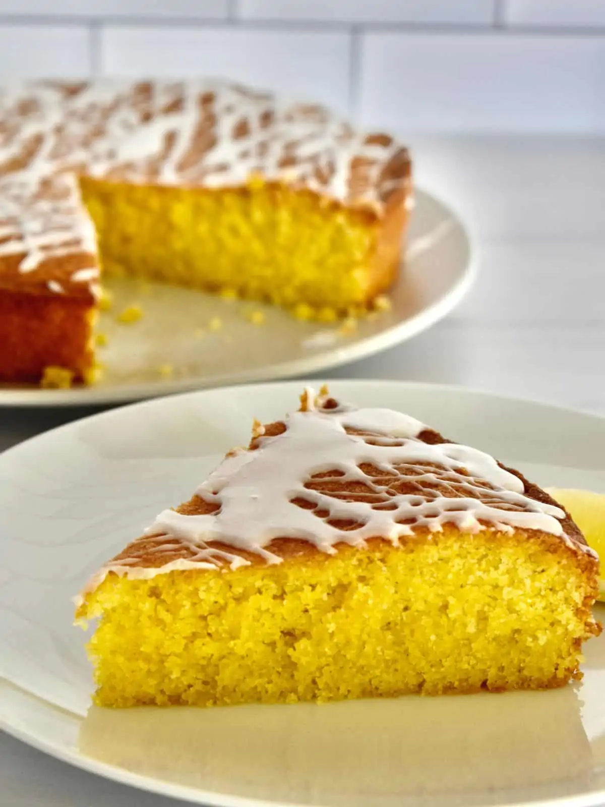 Lemon Polenta Cake slice on a white plate with the cake in the background.