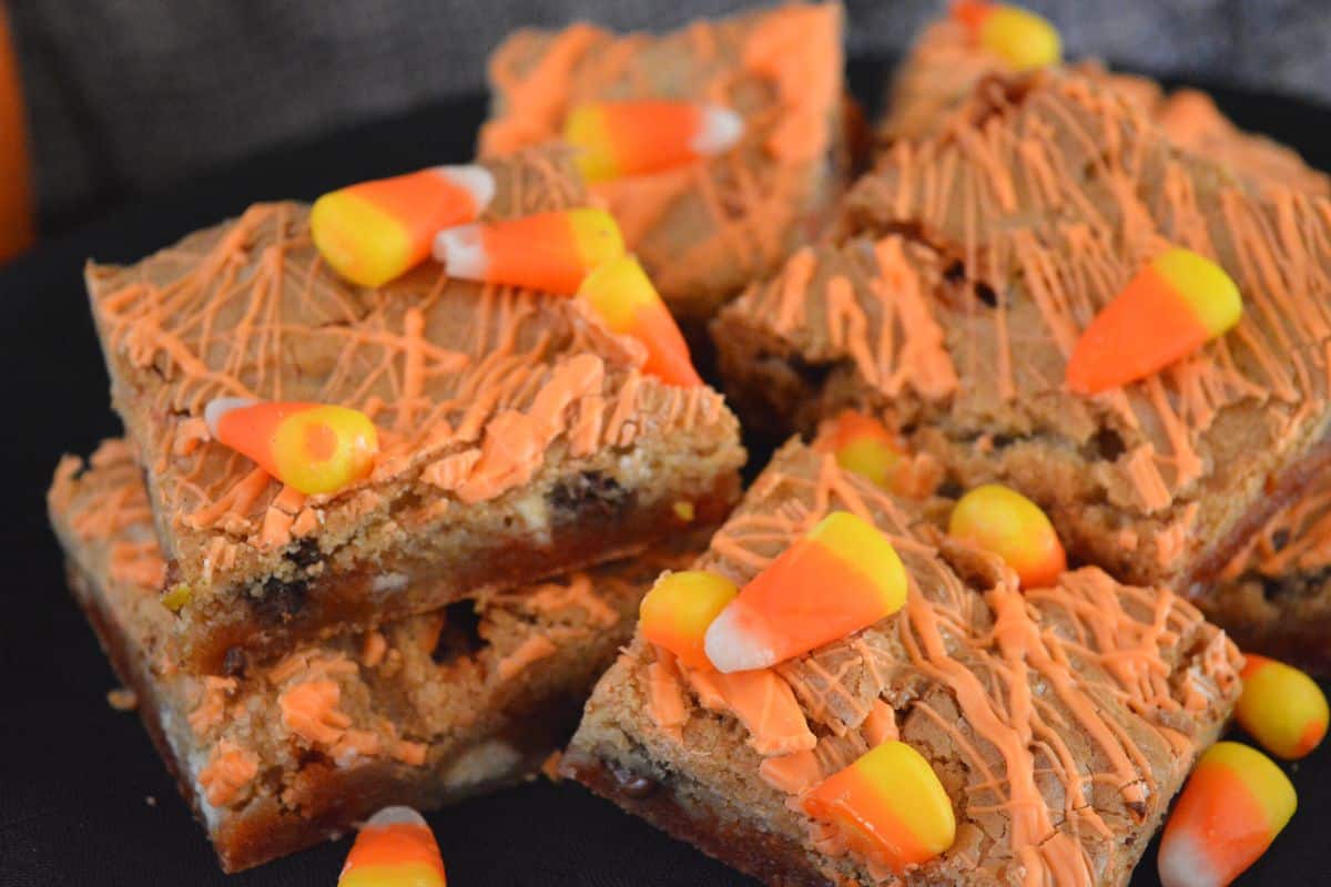 candy corn blondies with orange drizzle piled on each other with candy corn candies on top. 
