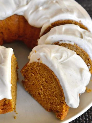 Pumpkin Bundt Cake with Cream Cheese Frosting on a plate with slices cut out of it.