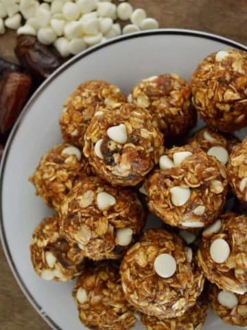 Pumpkin Protein Balls in a bowl with dates and white chocolate chips surrounding it.