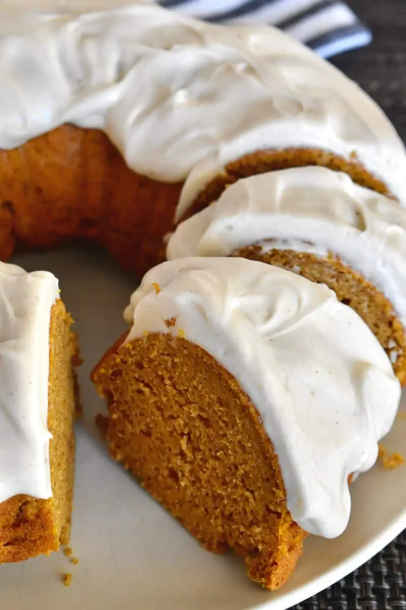Pumpkin Bundt Cake with Cream Cheese Frosting on a plate with slices cut out of it. 