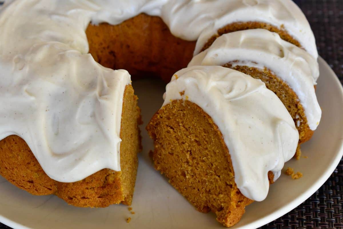 Pumpkin Bundt Cake with Cream Cheese Frosting on a plate with a slice of it cut. 