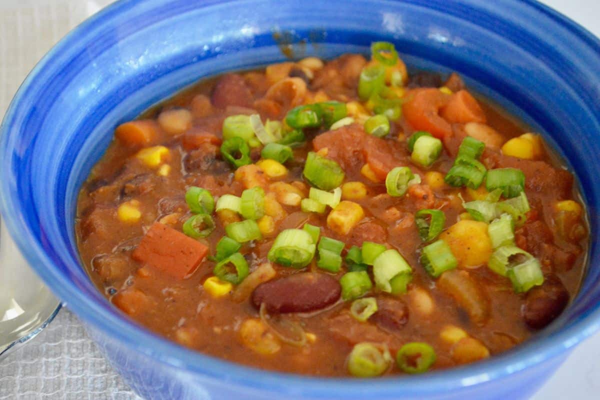 Three Bean Chili in a blue bowl with diced green onions on top. 