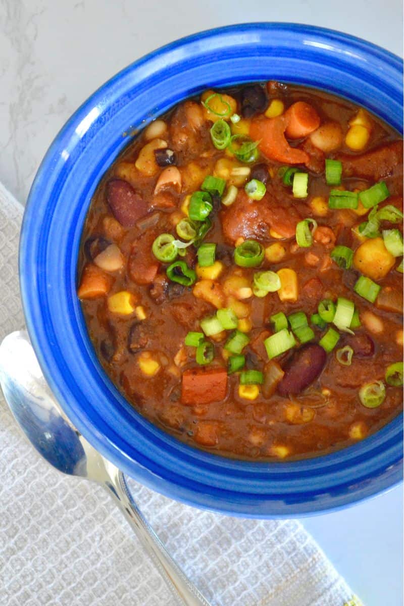 Three Bean Chili in a blue bowl with diced green onion on top.