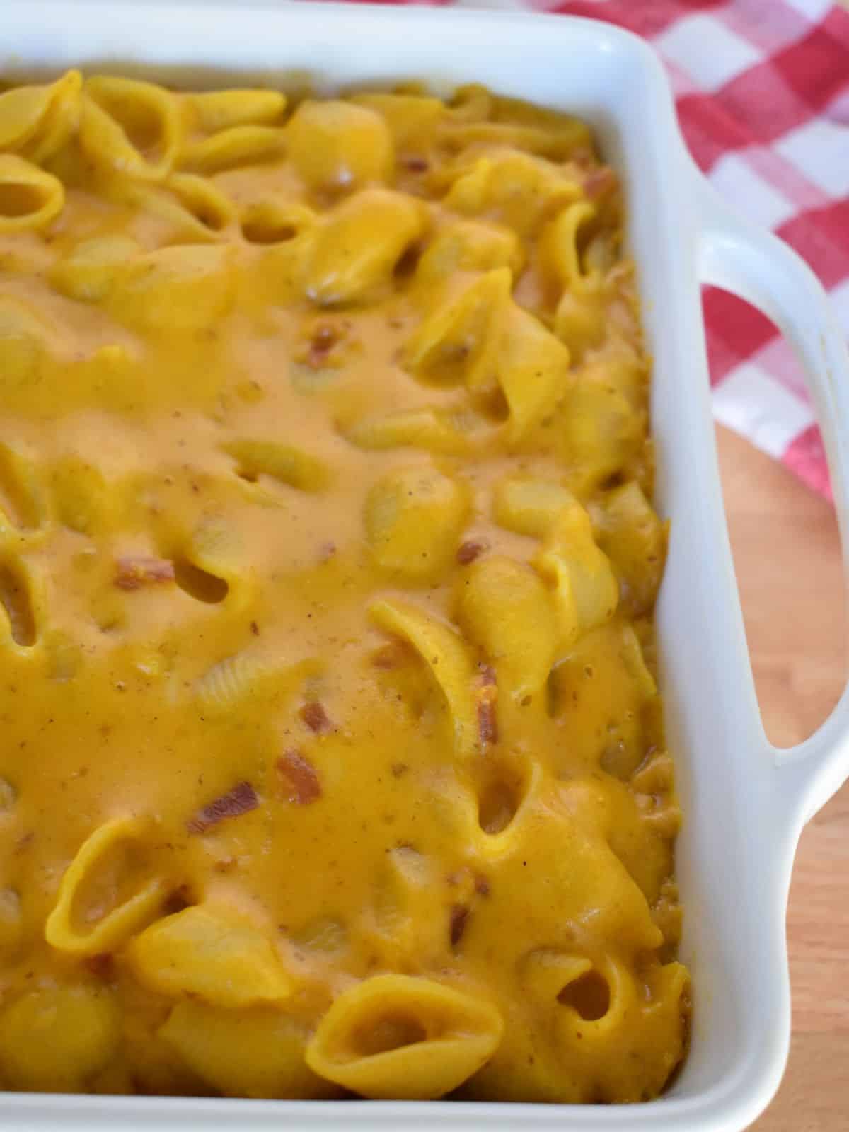 Pumpkin mac and cheese in a white casserole dish with a checkered napkin underneath. 