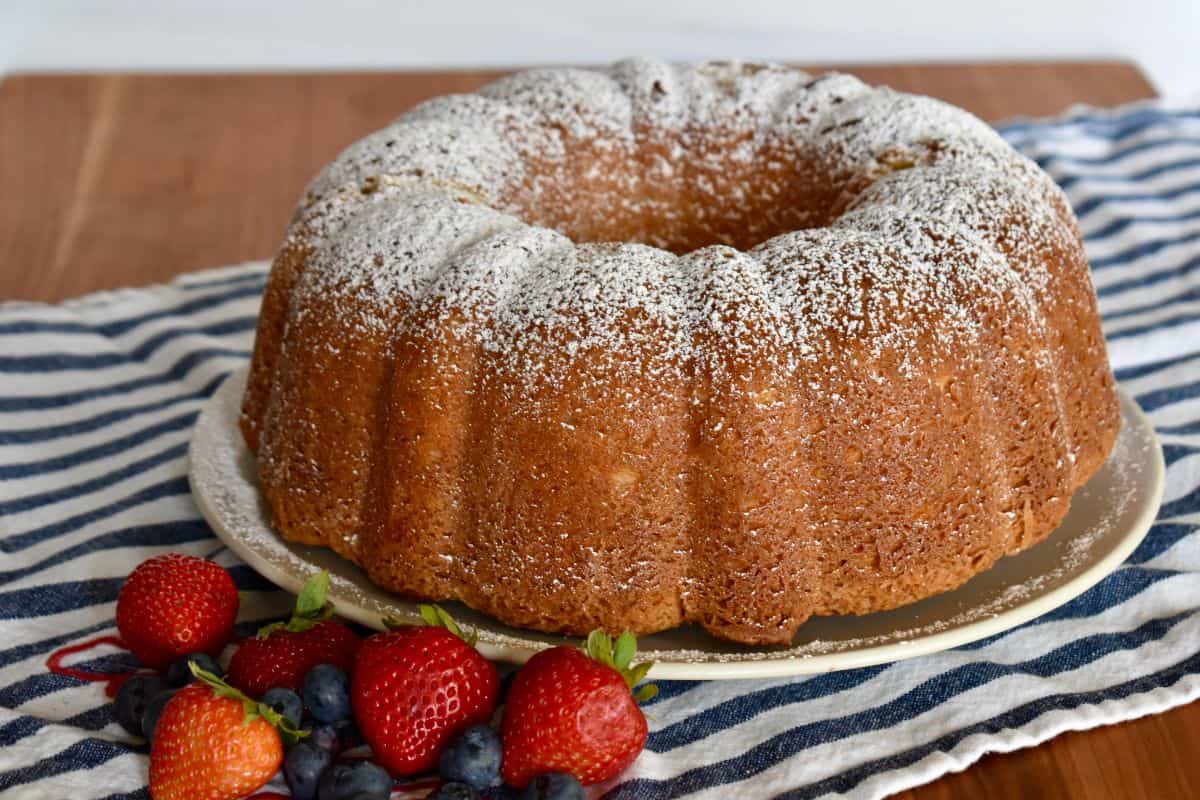 Sour Cream Pound Cake on a plate with powdered sugar dusted over top and berries on the side. 