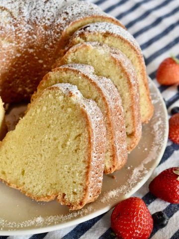 Sliced sour cream pound cake on a plate with a striped napkin and berries in the background.