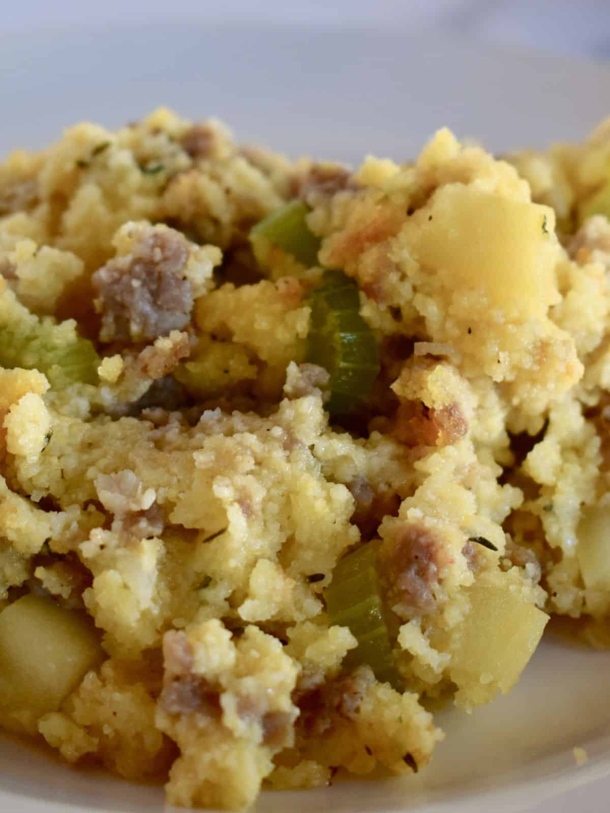 Cornbread stuffing with sausage and apple on a white plate. 