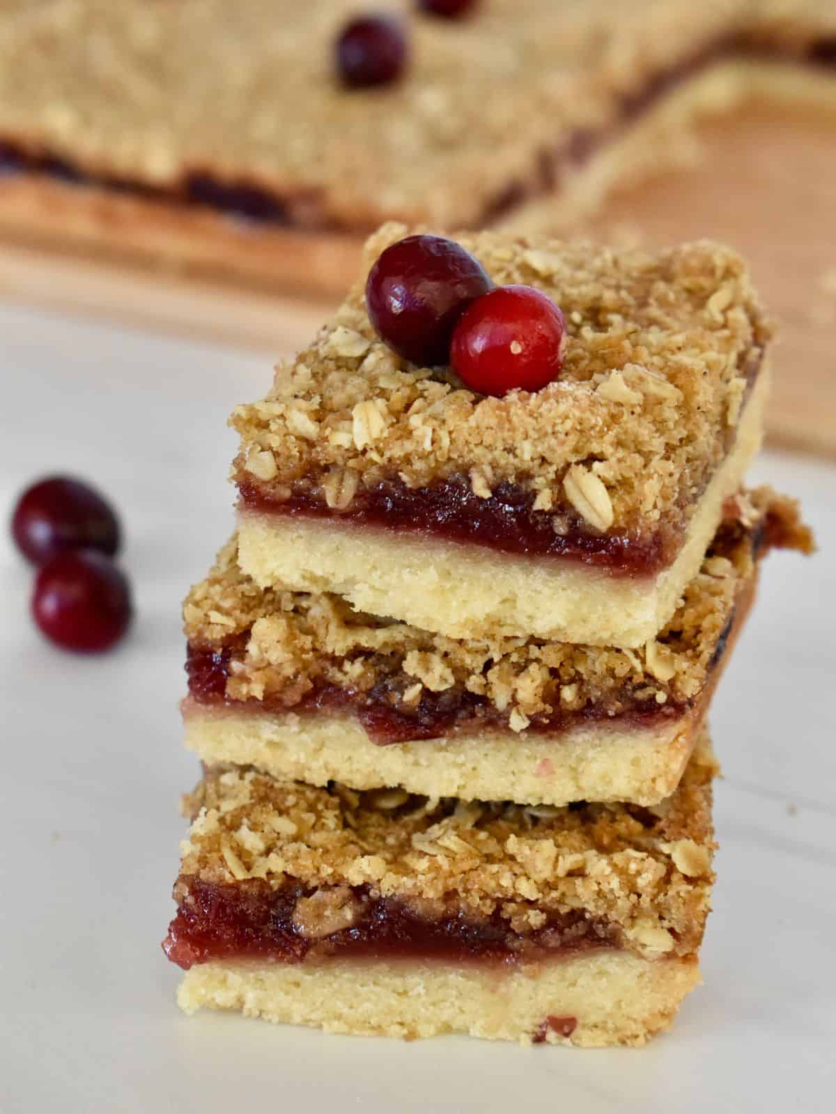 Cranberry Shortbread Bars stacked on each other on a countertop with cranberries in the background. 