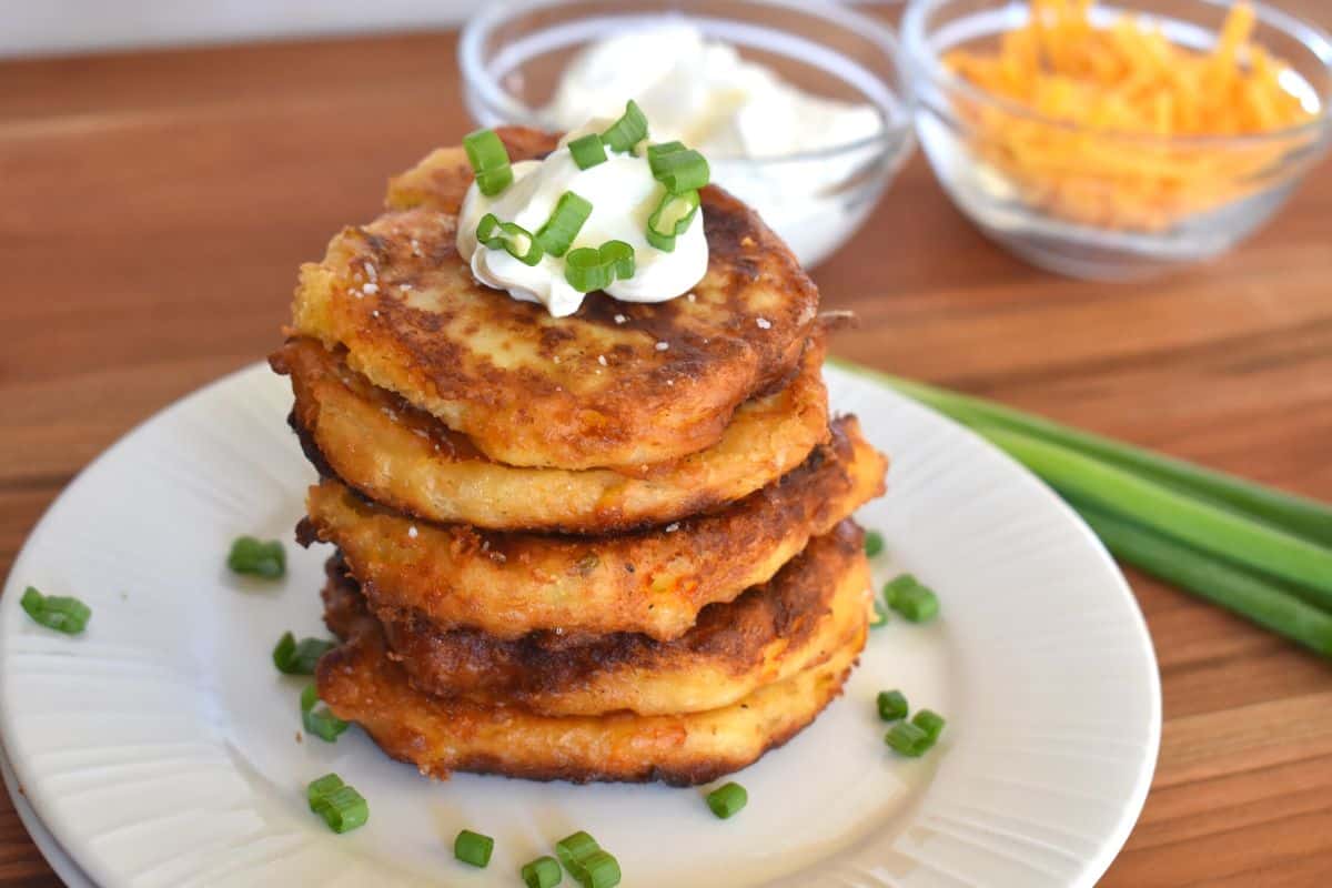 Mashed potato cakes on a white plate with sour cream on top and green onions scattered. 