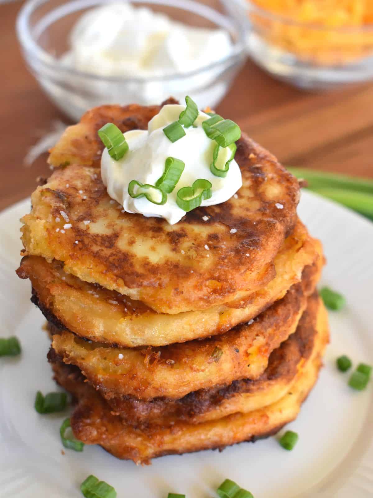Mashed Potato cakes stacked on each other on a plate with a dollop of whipped cream on top and green onions. 