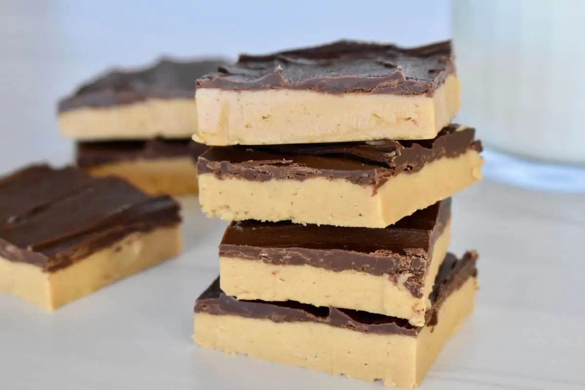 No Bake Chocolate Peanut Butter bars stacked on each other with a glass of milk in the background. 