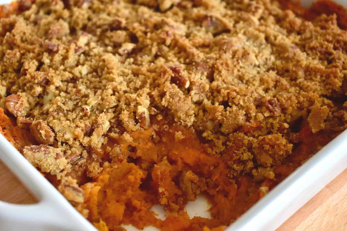Sweet Potato Casserole with Pecan Streusel in a white dish with a scoop taken out of it. 