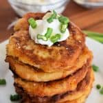 Mashed Potato Cakes stacked on each other on a white plate with sour cream on top.