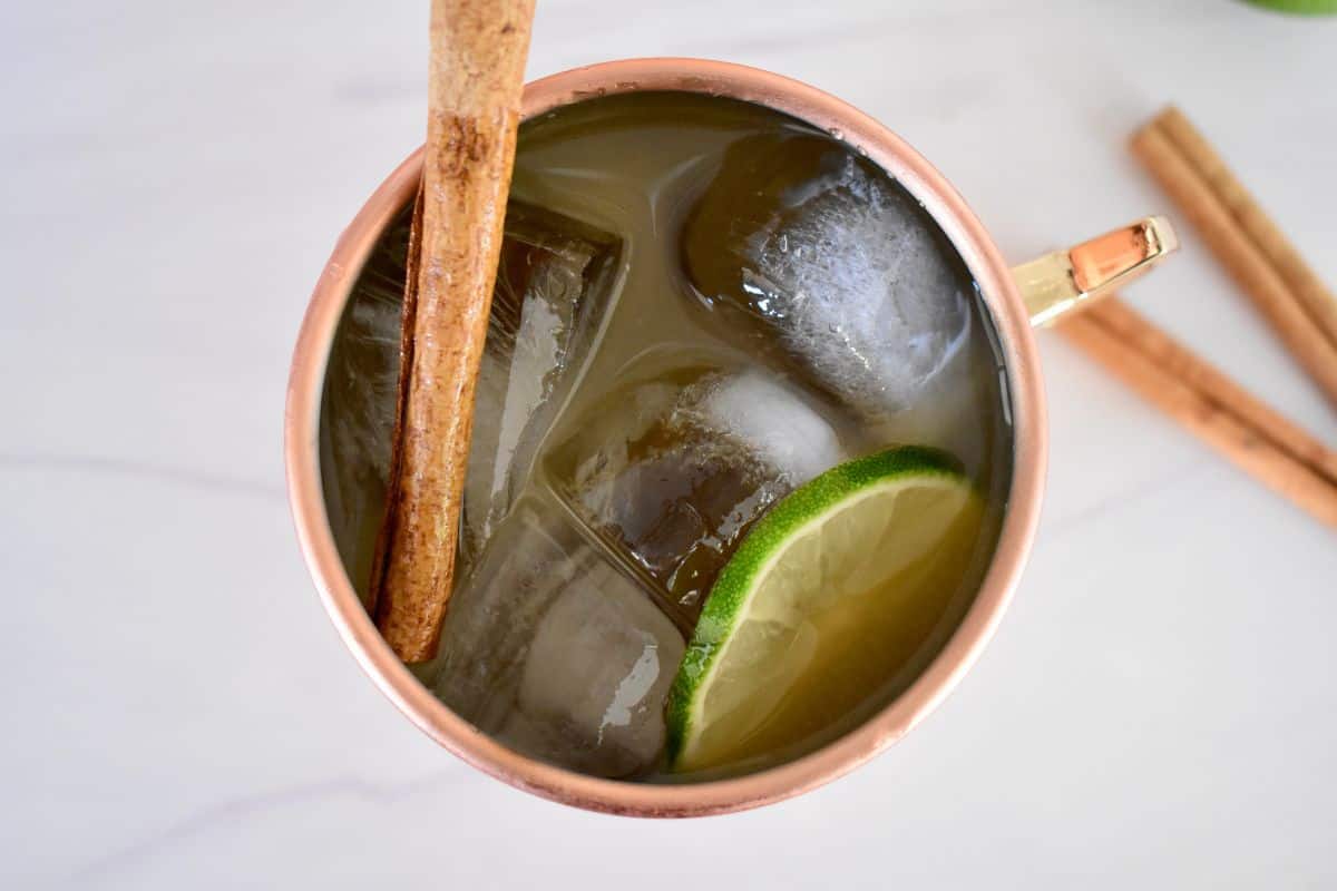overhead photo of drink in a copper mug with a lime wedge and cinnamon stick. 