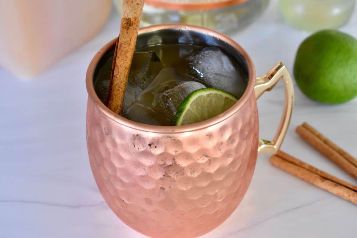 Apple Cider Moscow Mule in a cooper mug with a slice of lime and cinnamon stick garnish. 