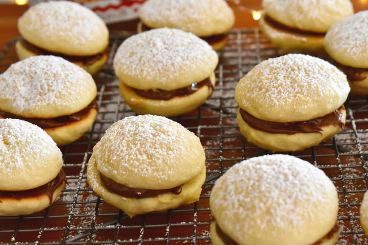 Nutella Sandwich Cookies on a wire baking rack with powdered sugar sprinkled over top. 