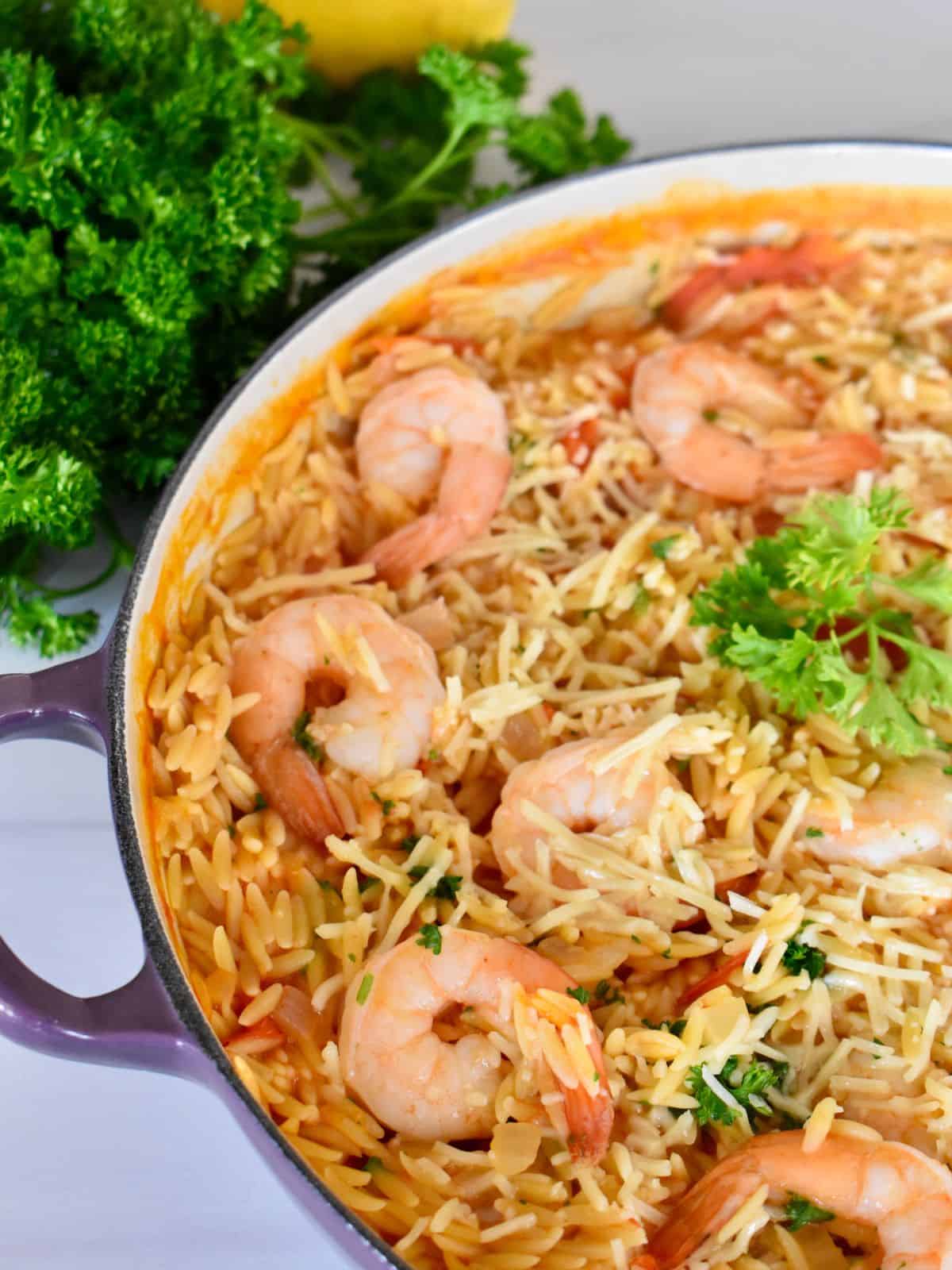 overhead photo of shrimp orzo in a large pot with parsley next to it. 