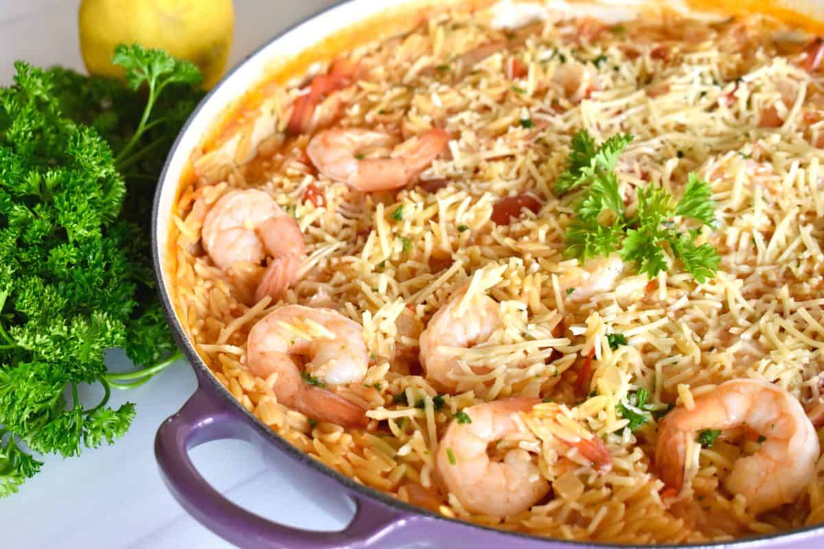 Shrimp Orzo in a pan with parsley and lemon next to it. 