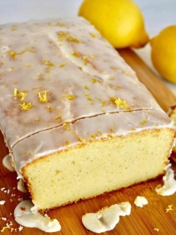 Lemon Ricotta Pound cake with glaze on a wood cutting board with a lemon in the background.