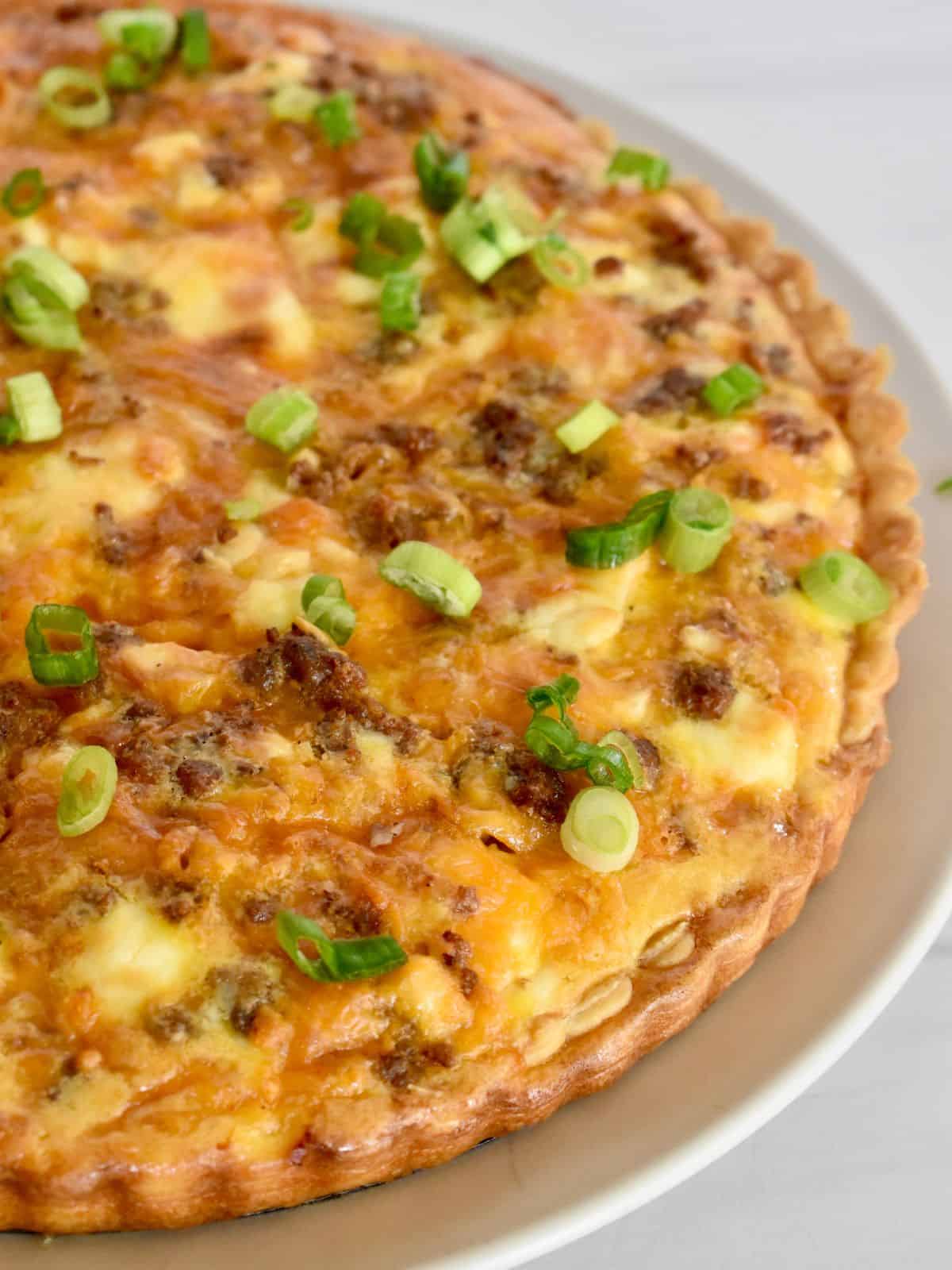 Breakfast tart with sausage and cheddar on a plate with green onion on top. 