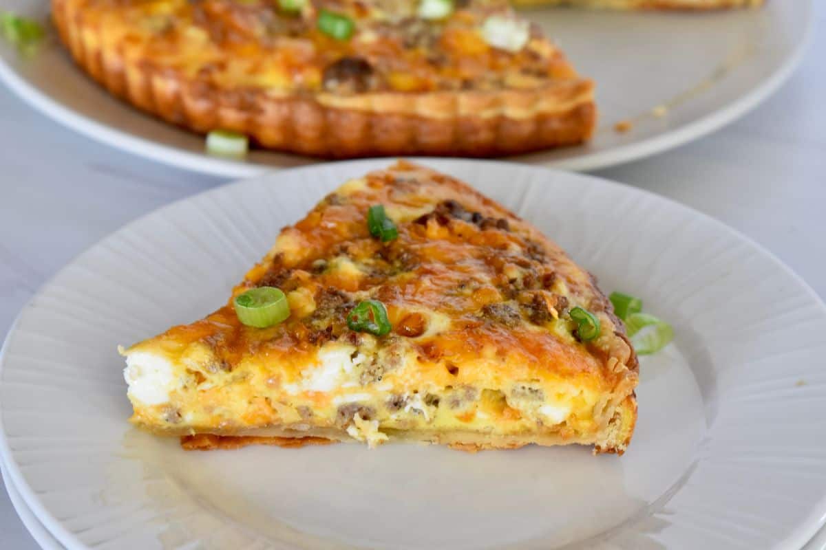 Slice of breakfast tart on a white plate with green onions on top. 