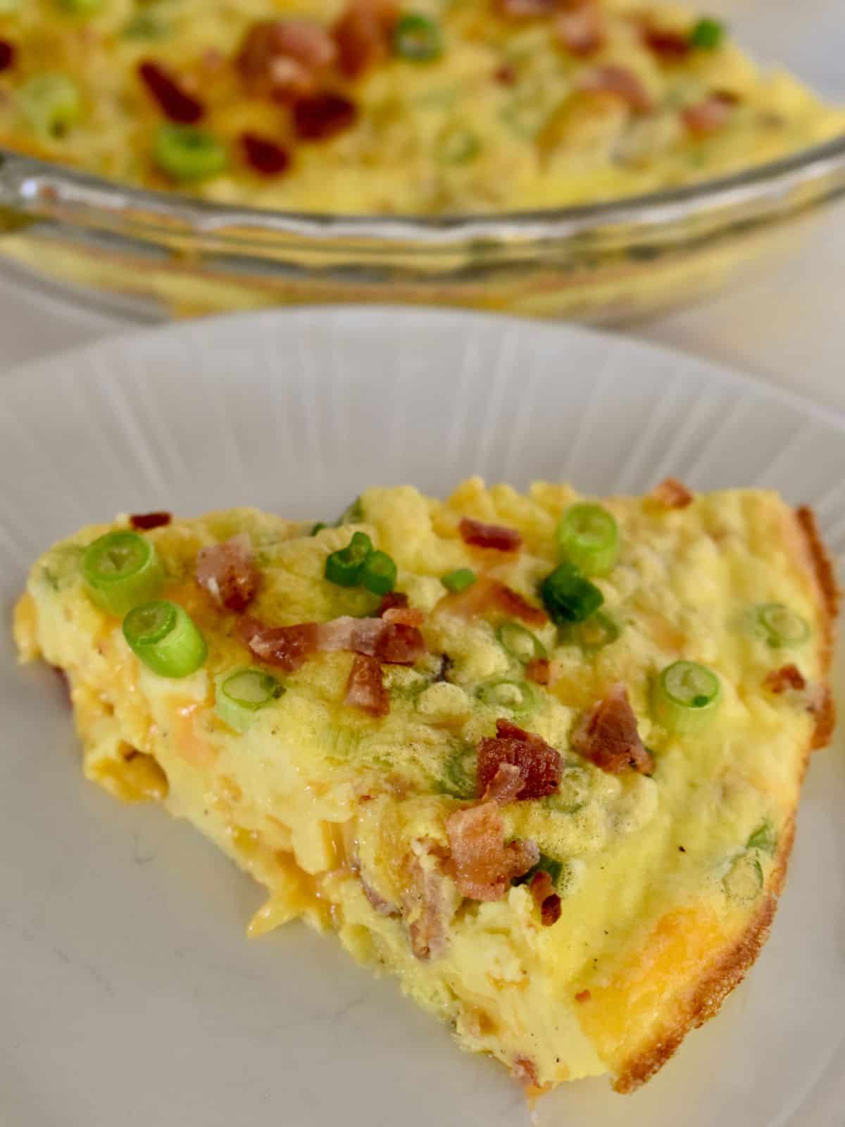 Slice of cottage cheese quiche on a white plate with bacon, cheese, and green onions. 