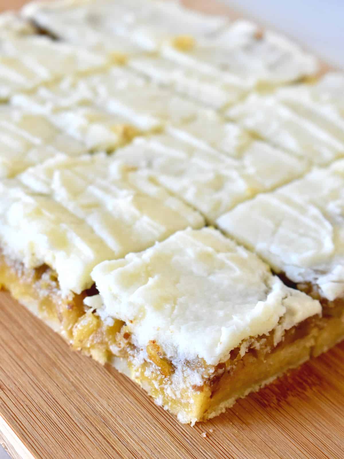 pineapple bars on a wood cutting board cut into squares. 