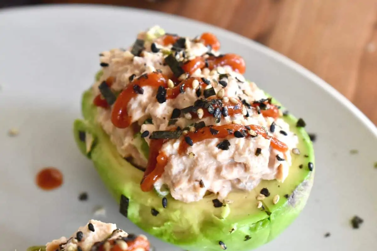 Salmon Stuffed Avocado on a plate with sriracha sauce drizzled on top. 