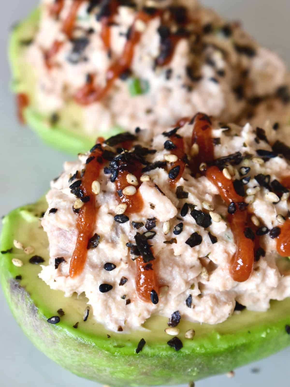 Salmon Stuffed Avocados on a plate with sriracha drizzle on top and furikake sprinkled on top. 