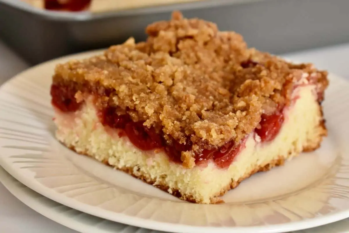 Slice of cherry coffee cake on a white plate. 