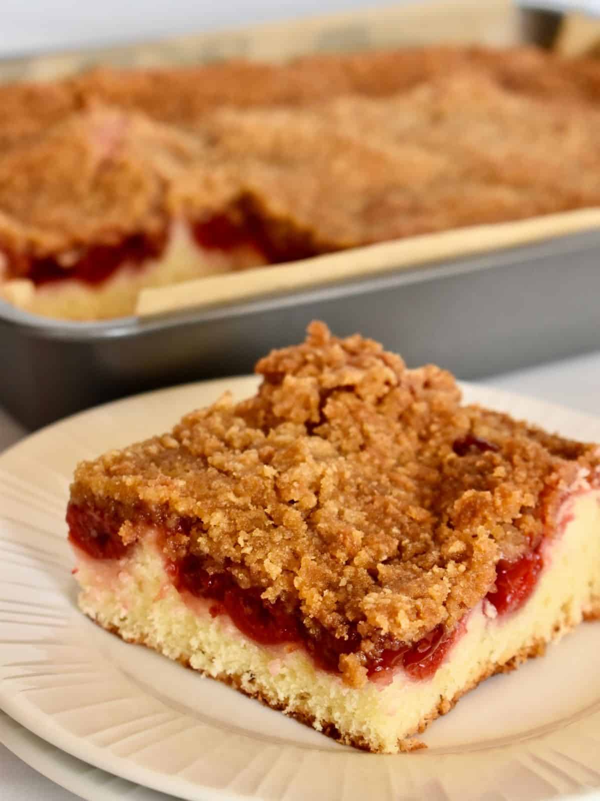 Cherry Coffee Cake with a slice on a plate and a pan of coffee cake in the background. 