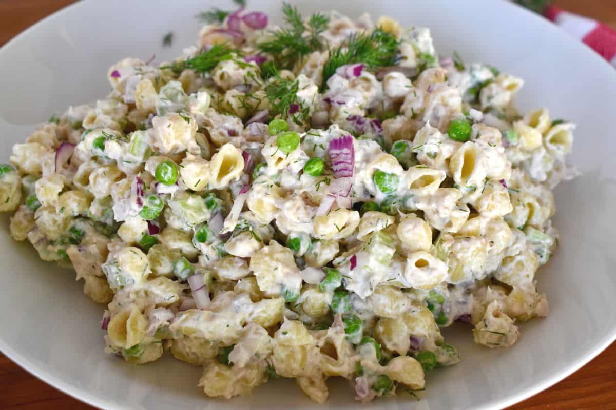 Tuna pasta salad with dill in a white bowl with a checkered napkin in the background. 