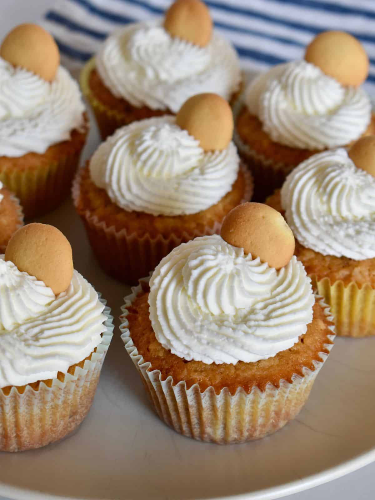 Vanilla wafer cupcakes on a plate with a vanilla wafer on top and a striped cloth in the background. 
