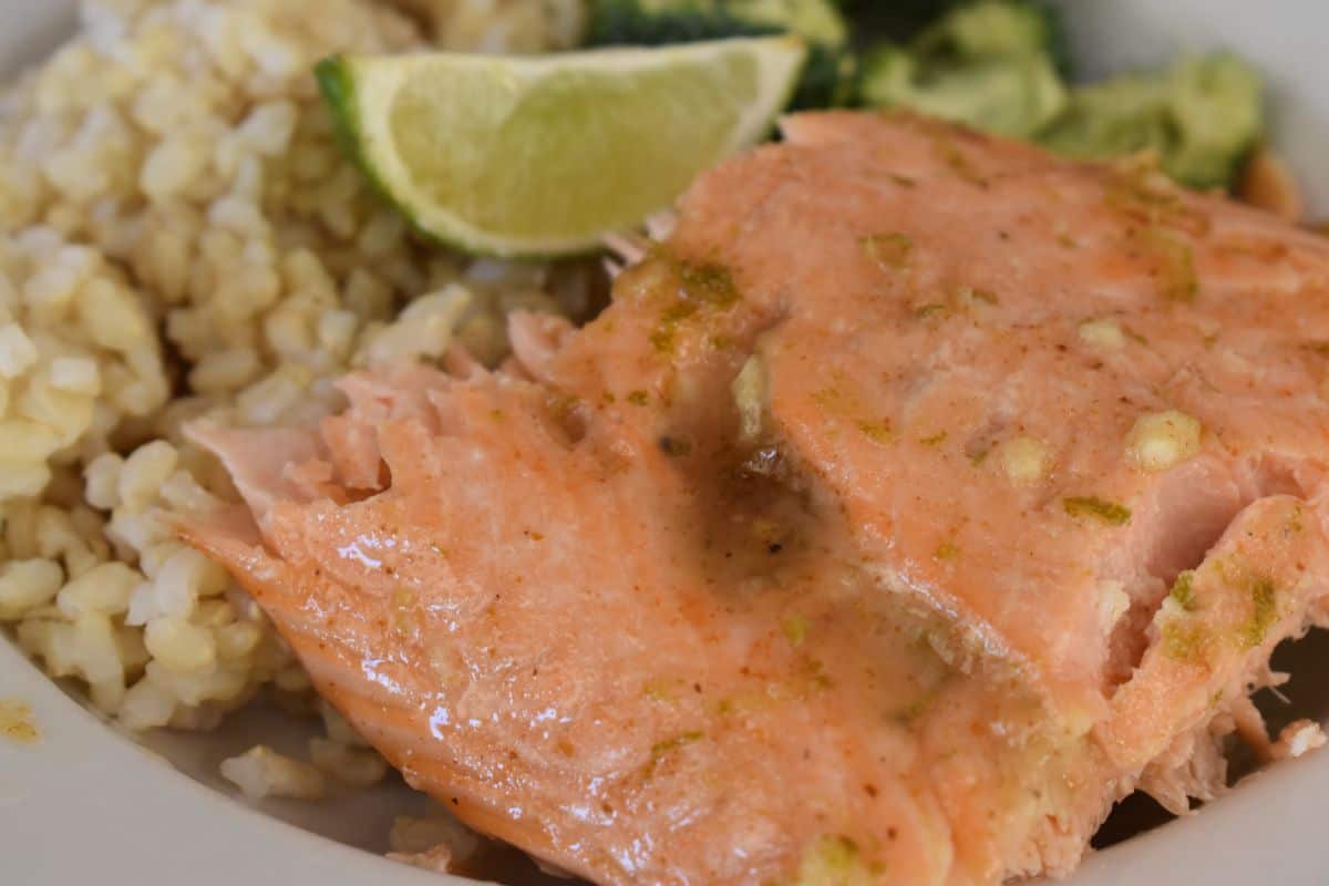baked salmon on a white plate with a lime wedge, brown rice, and broccoli. 