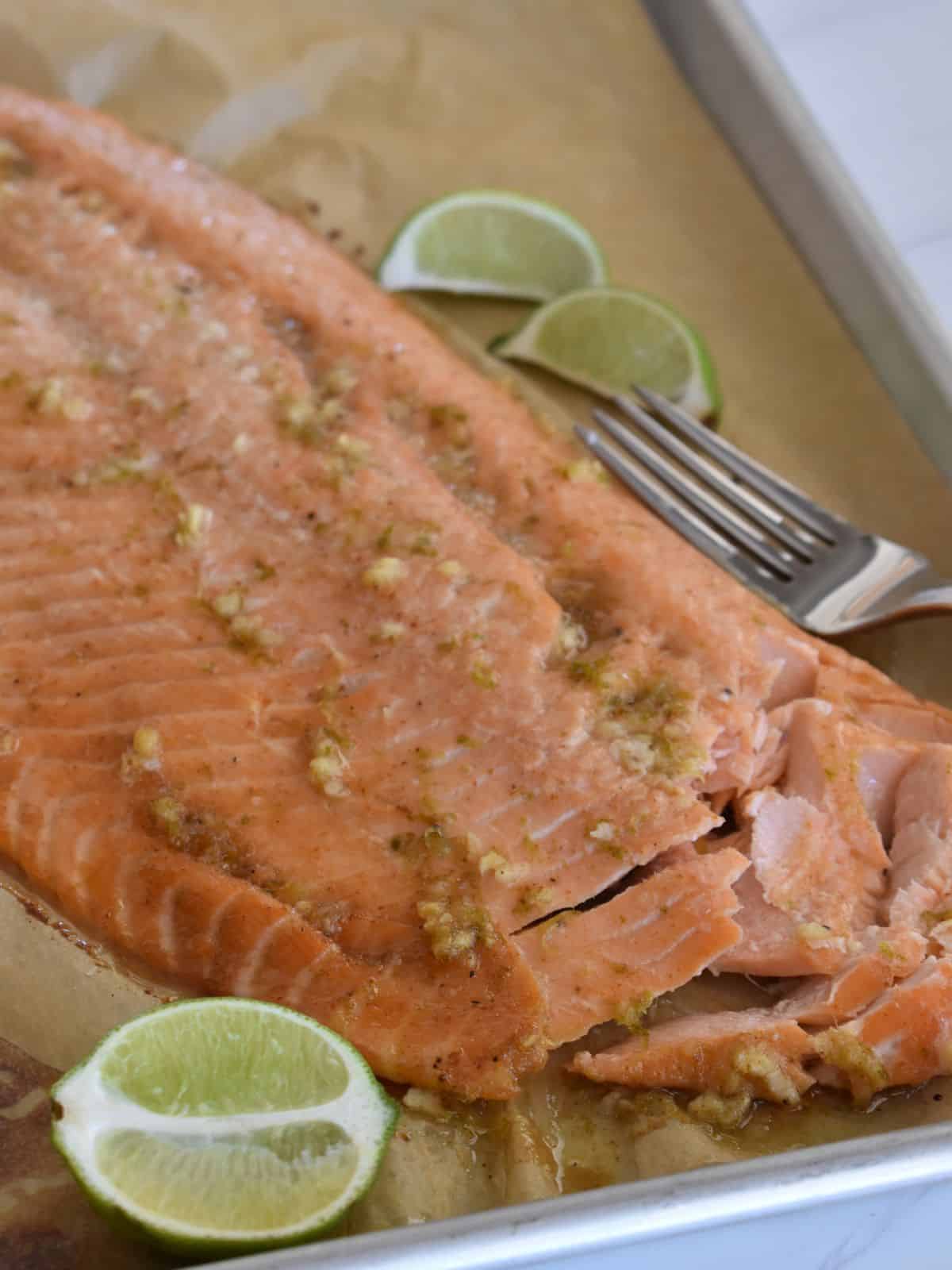 Honey Lime Salmon on parchment lined baking sheet with limes next to it. 