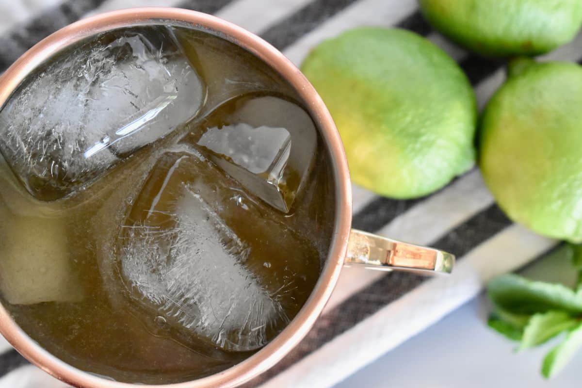 overhead photo of drink in a copper mug with limes in the background. 
