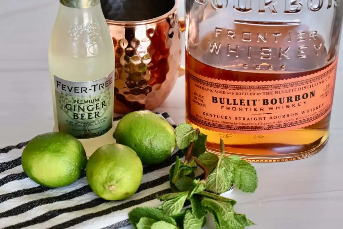 ingredients needed to make drink including ginger beer, bourbon, limes, and fresh mint. 