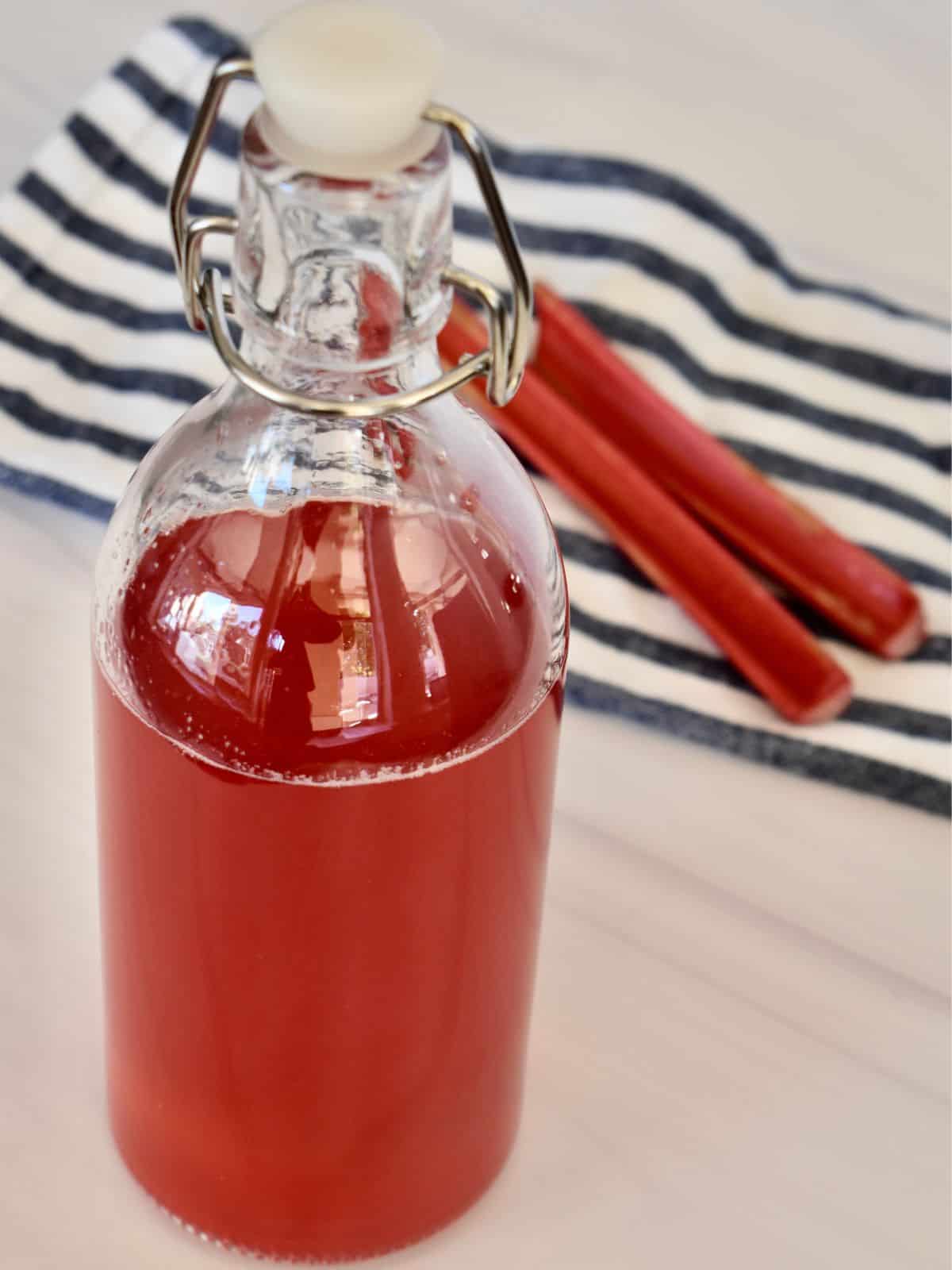 Rhubarb Simple Syrup in a glass bottle with fresh rhubarb behind it. 