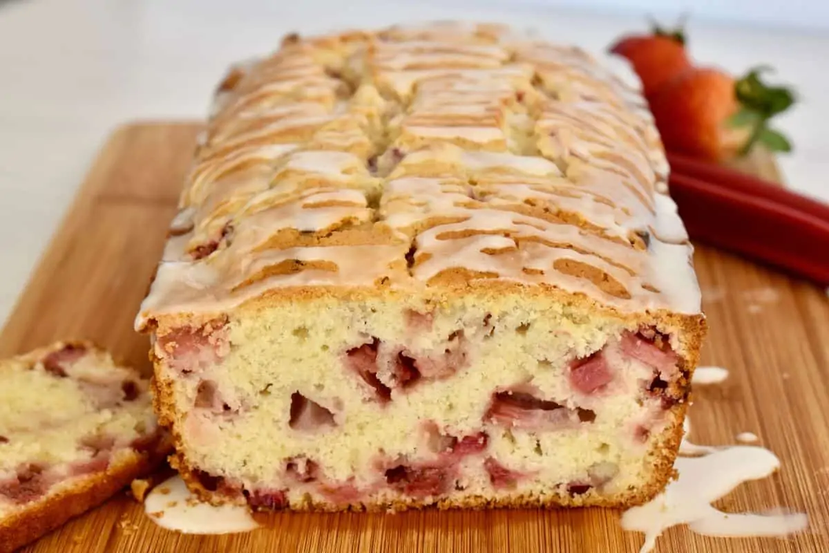 Strawberry Rhubarb Bread with a slice cut off on the end and strawberries in the background. 