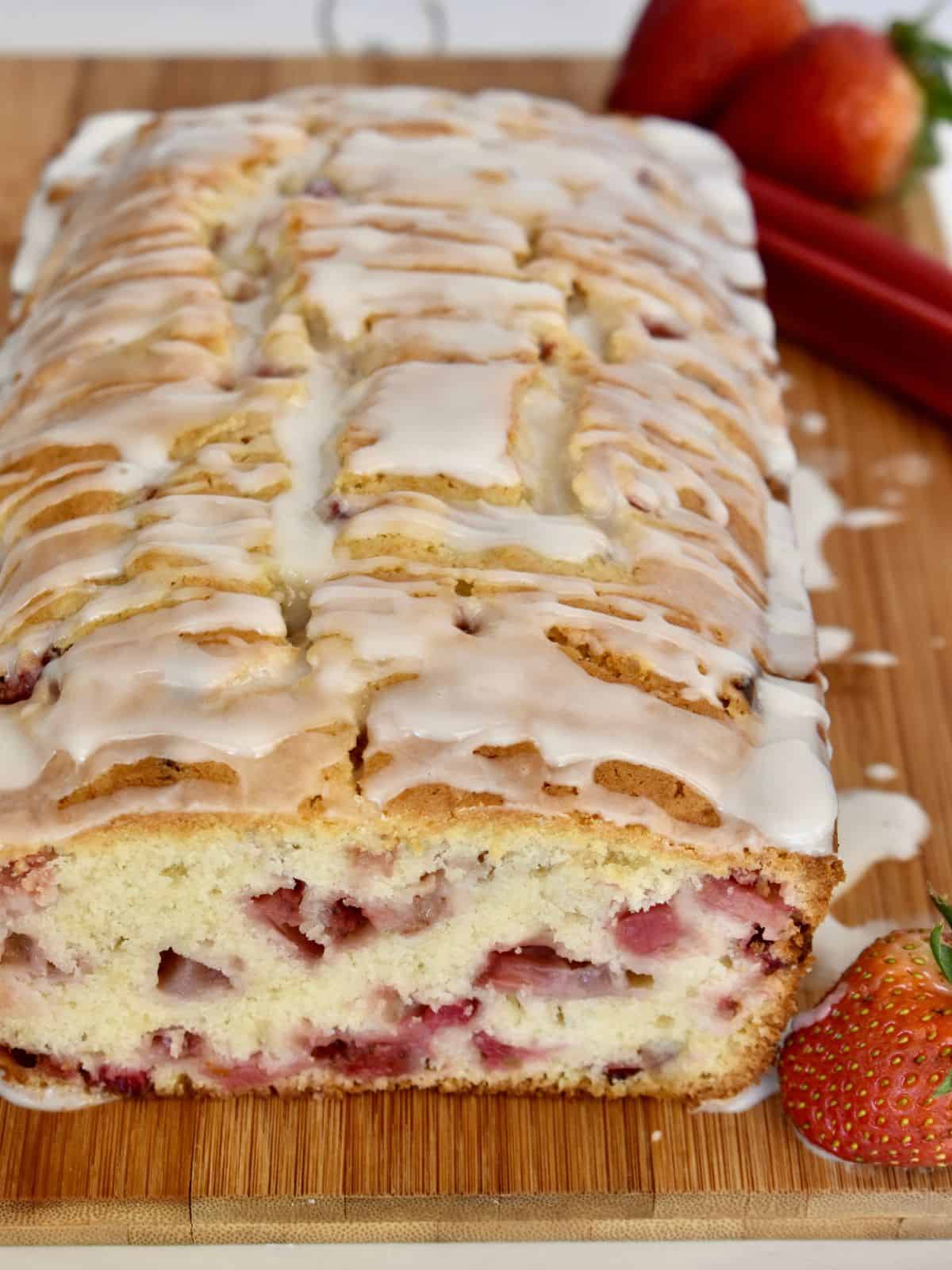 Strawberry Rhubarb Bread on a wood cutting board with a white glaze on top. 