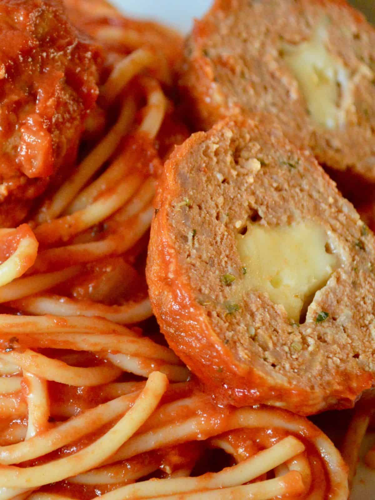 Stuffed turkey meatballs with a cheese center on a plate of spaghetti and marinara sauce. 