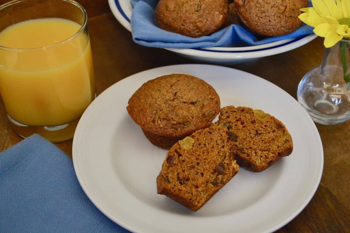 Carrot Date Muffins on a white plate with a glass of orange juice and blue napkin in the background. 