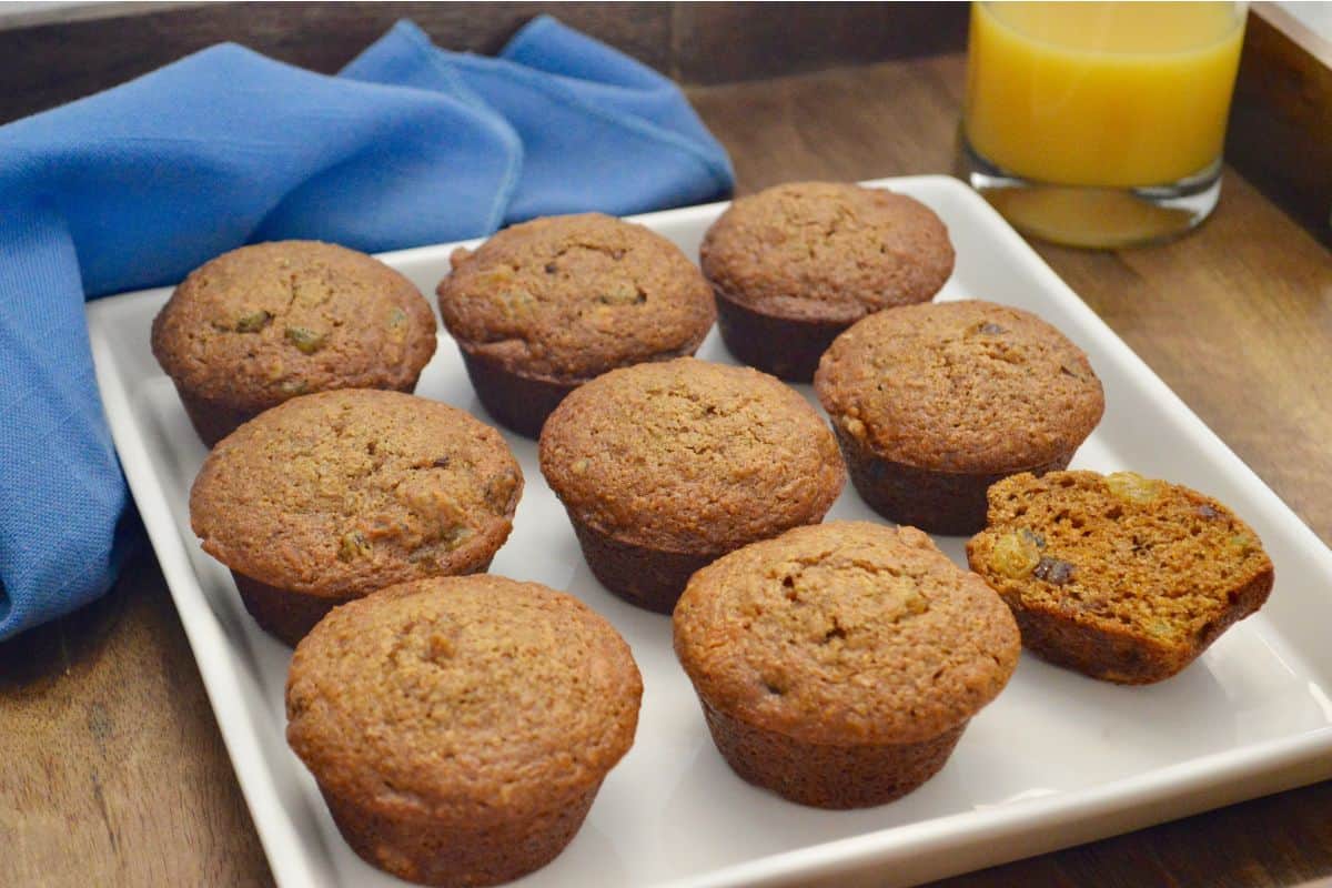Carrot Date Muffins on a white serving plate with a glass of orange juice in the background. 