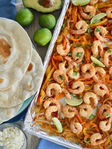 overhead photo of sheet pan shrimp fajitas with tortillas and lime next to it.