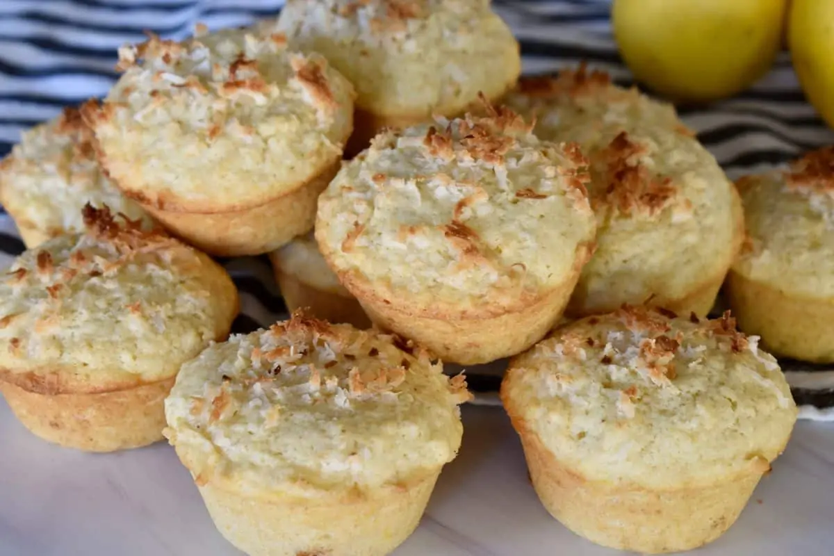 Stack of lemon coconut muffins on a white board with a striped napkin in the background. 